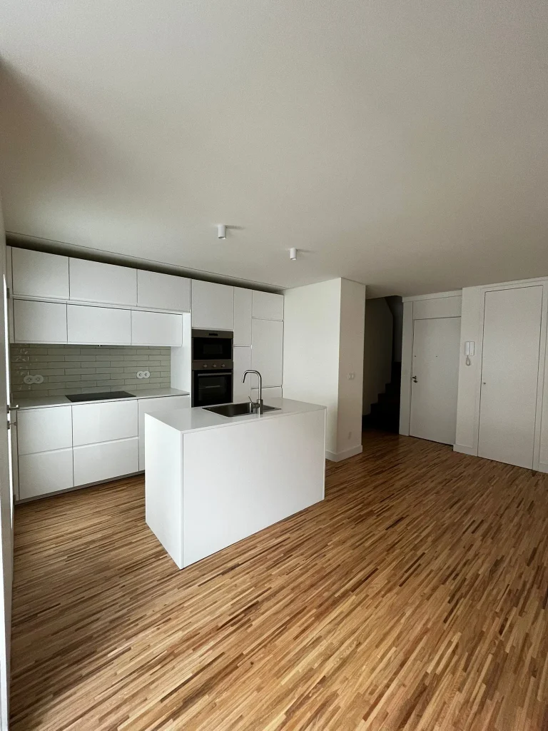 Imagem de uma cozinha completamente remodelada, com design moderno e funcional. A cozinha apresenta armários de linhas clean, bancadas de acabamento elegante, e electrodomésticos de última geração. O espaço é amplo e bem iluminado, com detalhes que valorizam a estética e a praticidade do ambiente.