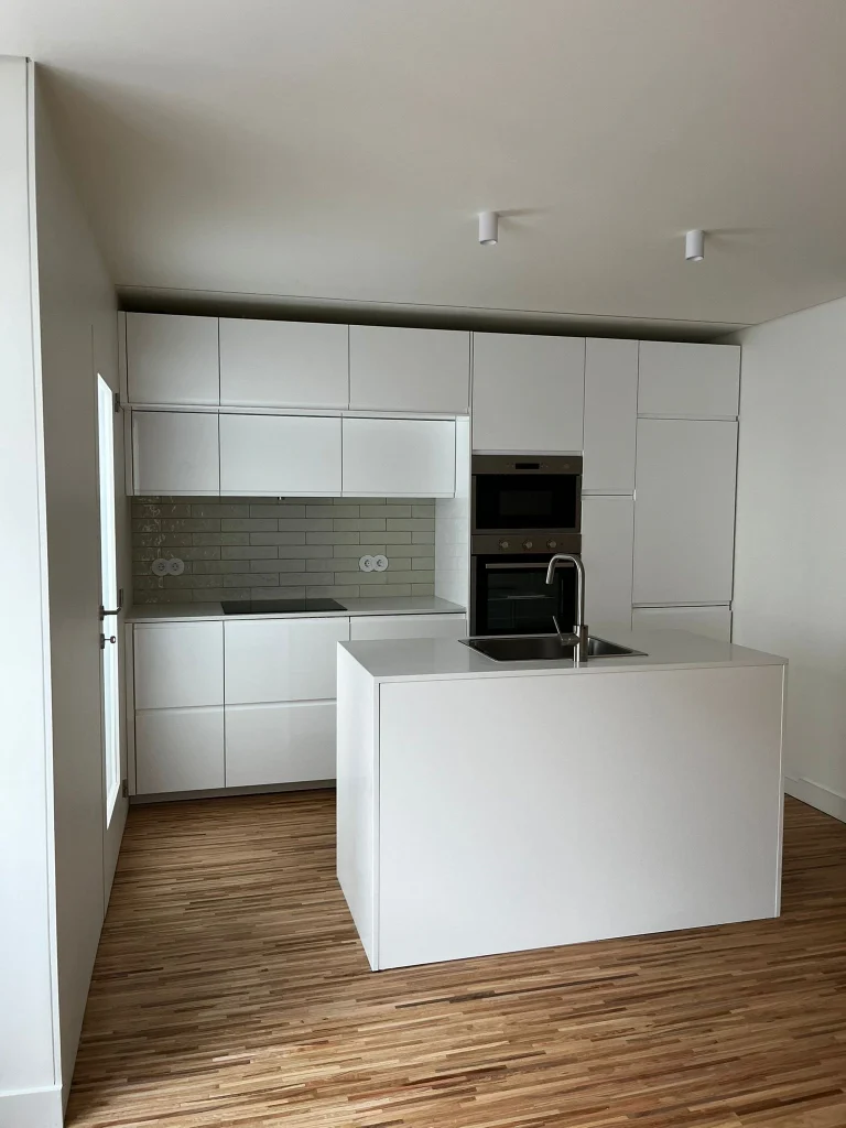 Imagem de uma cozinha completamente remodelada, com design moderno e funcional. A cozinha apresenta armários de linhas clean, bancadas de acabamento elegante, e electrodomésticos de última geração. O espaço é amplo e bem iluminado, com detalhes que valorizam a estética e a praticidade do ambiente.