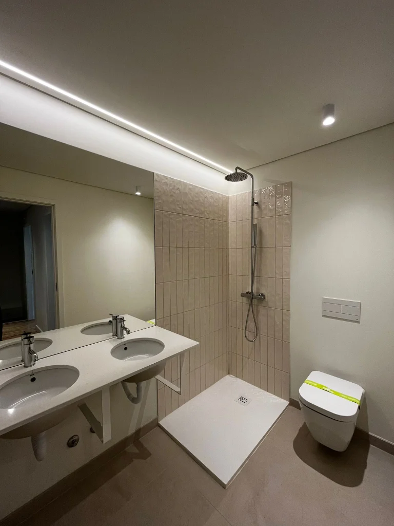 Imagem de uma casa de banho pequena completamente remodelada, com design moderno e funcional. Apresenta zona de duche e lavatório branco e acabamento elegante.