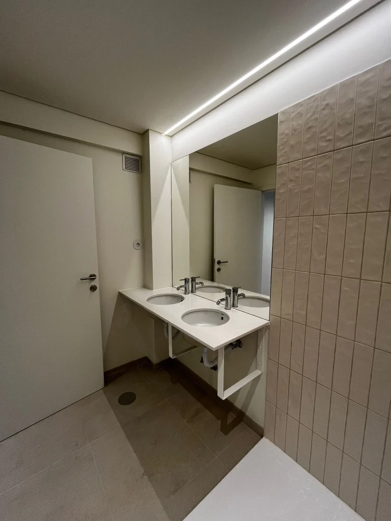 Imagem de uma casa de banho pequena completamente remodelada, com design moderno e funcional. Apresenta zona de duche e lavatório branco e acabamento elegante.