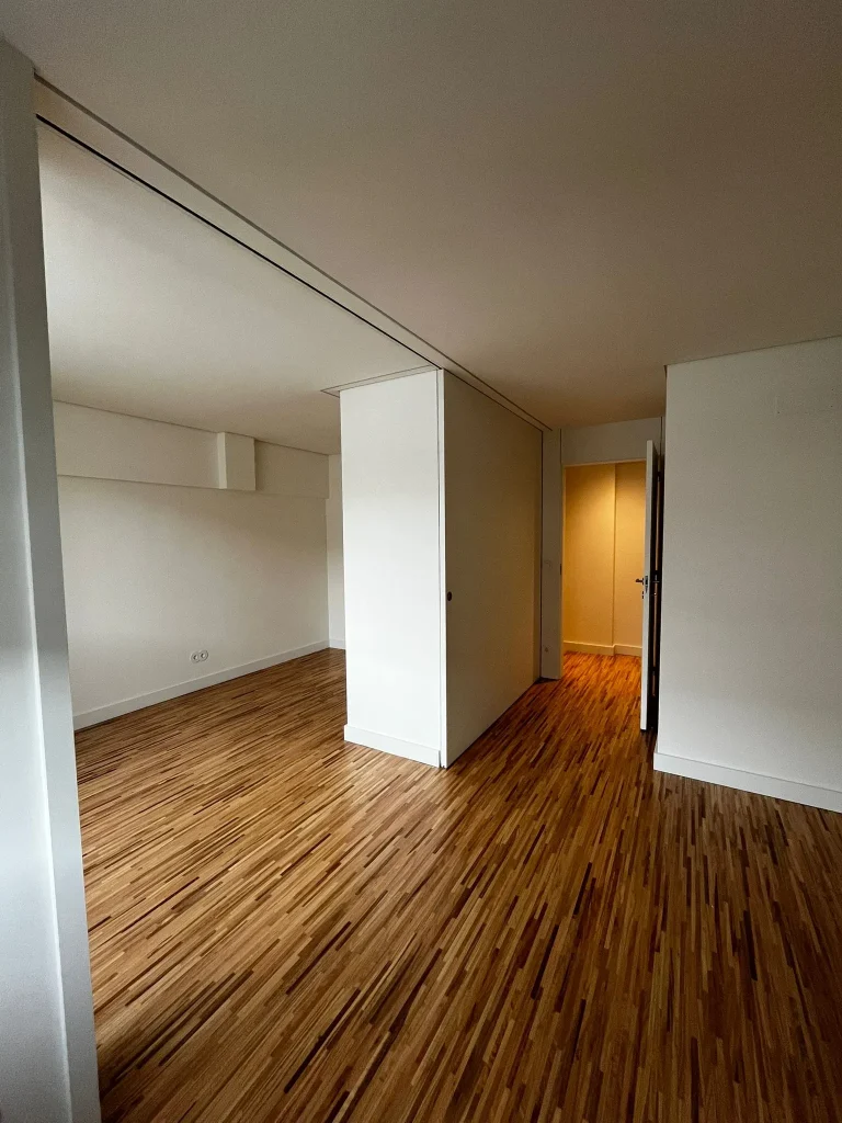 Imagem de quartos amplos com pavimento em taco de madeira, destacando o ambiente acolhedor e elegante. A disposição do espaço privilegia a luminosidade natural, enquanto o revestimento confere um toque intemporal e confortável, combinando funcionalidade e estética.