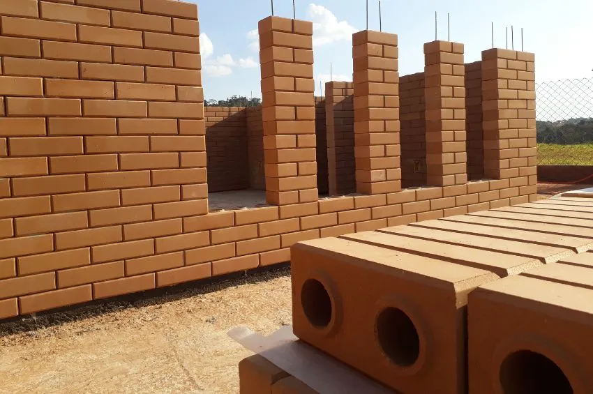 Esta imagem mostra um canteiro de obras utilizando tijolos ecológicos de solo-cimento (também conhecidos como tijolos de encaixe ou tijolos prensados). Esses tijolos são feitos a partir de uma mistura de solo, cimento e água, compactados sob alta pressão e geralmente curados ao invés de queimados, tornando-os uma opção mais sustentável para a construção. Você gostaria de saber mais sobre os benefícios, técnicas de construção ou comparações de custo desses tijolos?