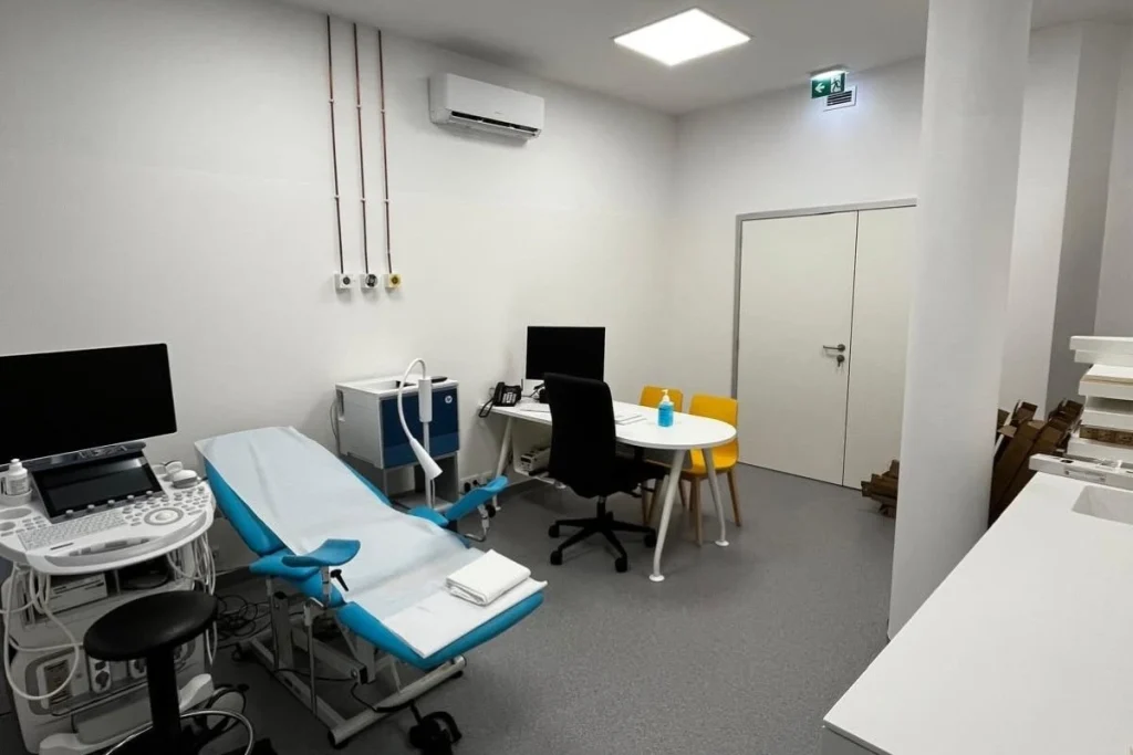 Sala de diagnóstico equipada com ecógrafo, marquesa azul e branca, mesa com computador e cadeiras; inclui tomadas técnicas, pontos de gases medicinais e iluminação clínica, transmitindo organização e prontidão para exames.